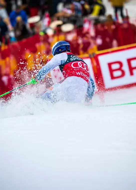 Professional alpine ski racer in action during the Lauberhorn downhill race in Wengen, carving through powder snow at high speed with Wendy's sponsorship barriers visible, capturing the intensity of FIS World Cup skiing competition