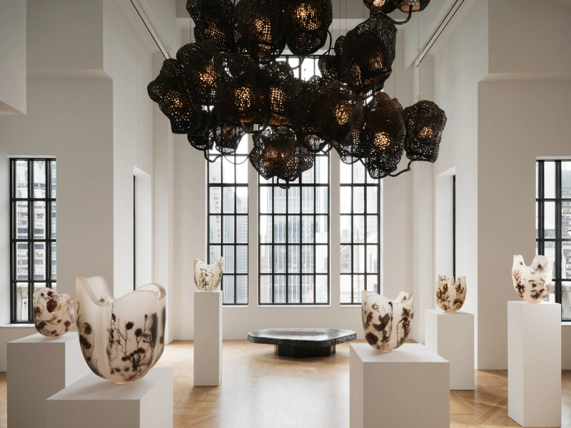 Carpenters Workshop Gallery presentation at Zonamaco Forma 2026 featuring dramatic black perforated sculptural chandelier suspended above organic ceramic vessels displayed on white pedestals in minimalist gallery space with natural light.