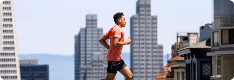 Man running outdoors in athletic wear with tall city buildings in the background.