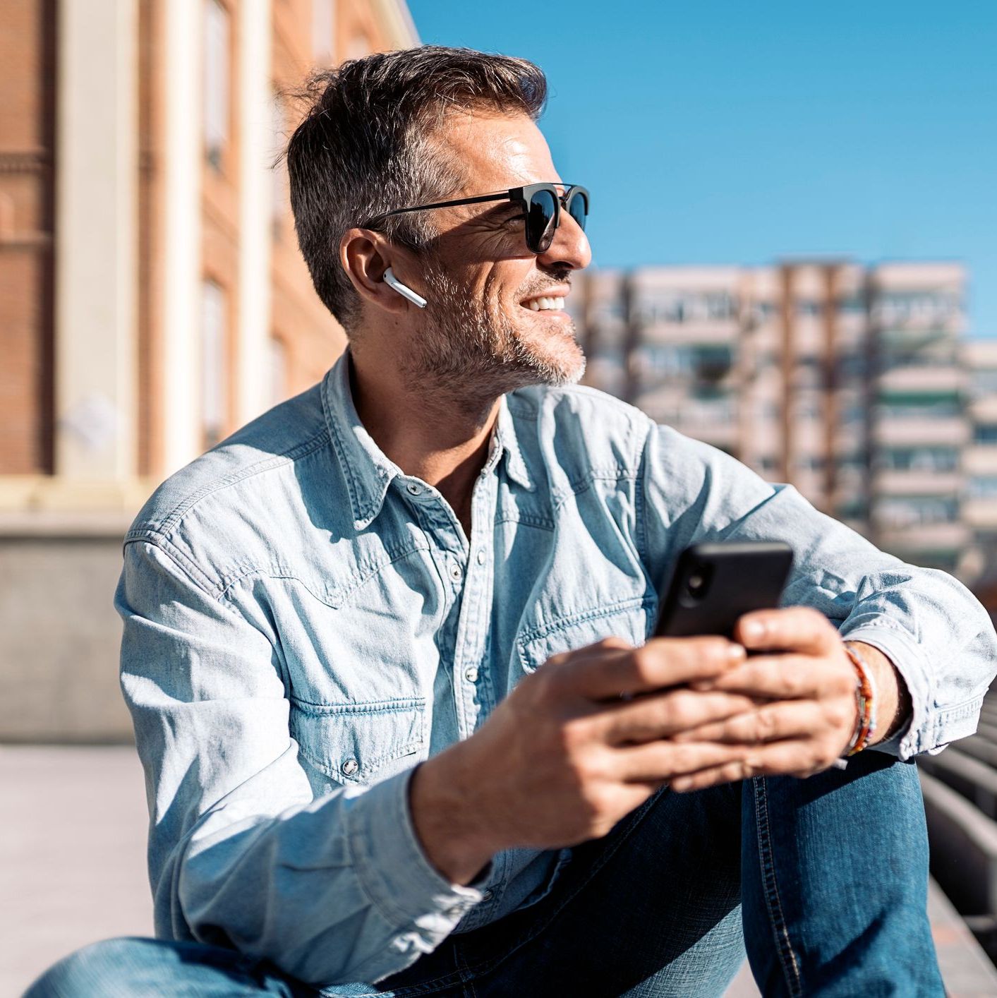 Smiling middle-aged man with gray hair and glasses walking in a city, wearing a backpack and casual clothes.
