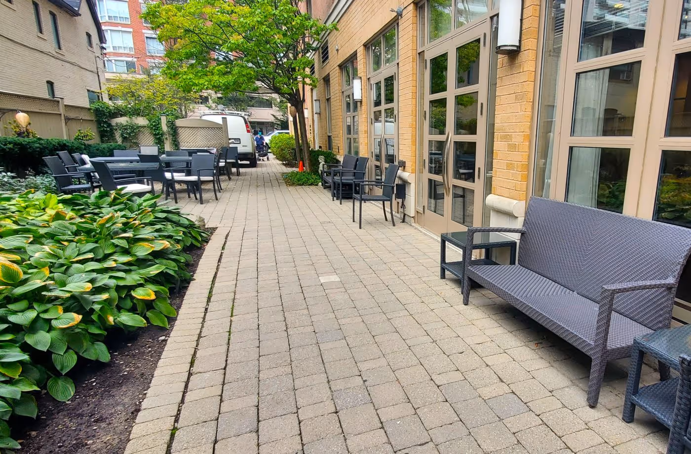 Clean patio stones well maintained next to flower bed full of annuals. Creeping plants make its way up the pergola behind the outdoor seating area.