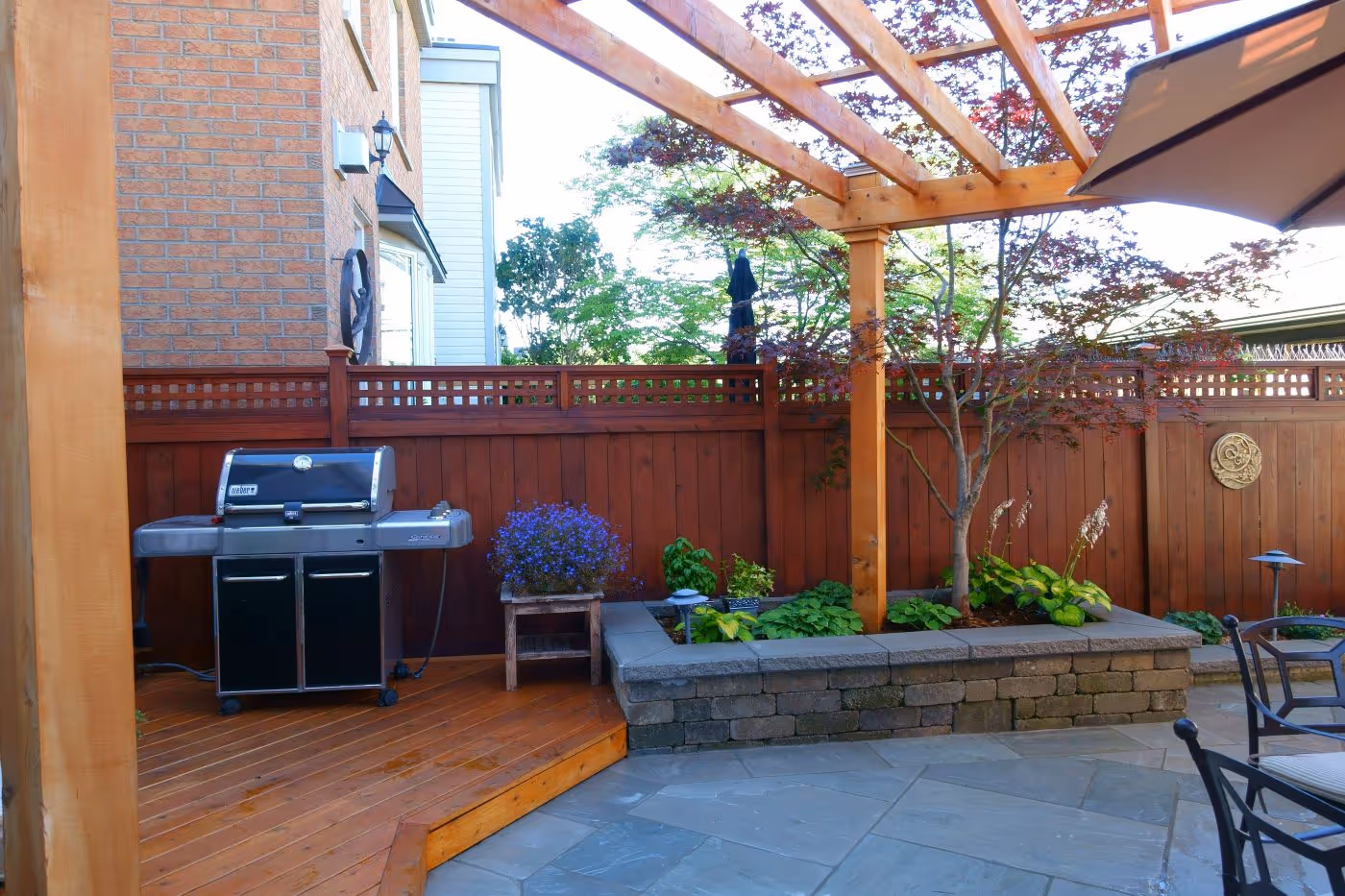 Wood Deck with BBQ leading to stone patio separating backyard elements