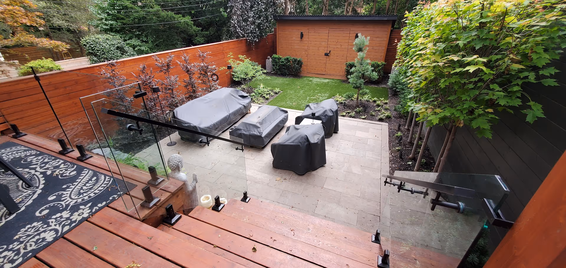View looking from upper deck to lower patio. Showcasing new trees and outdoor spaces