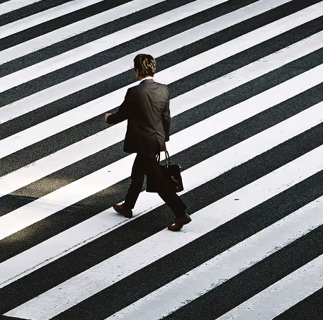 Person in a suit carrying a briefcase walking across a striped crosswalk.