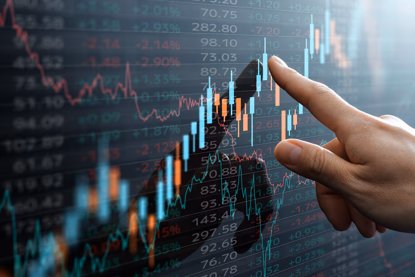 Hand pointing at a digital financial chart with colorful candlestick and line graphs displaying stock market data.