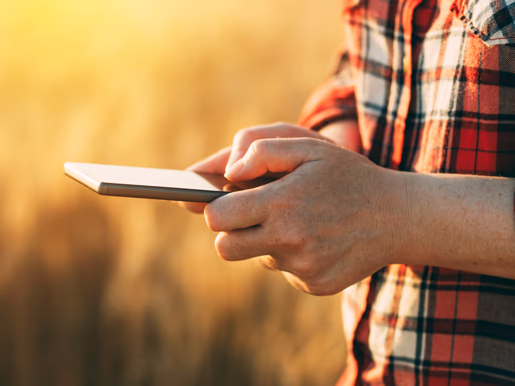 Person in a red plaid shirt using a tablet outdoors with soft sunlight in the background.