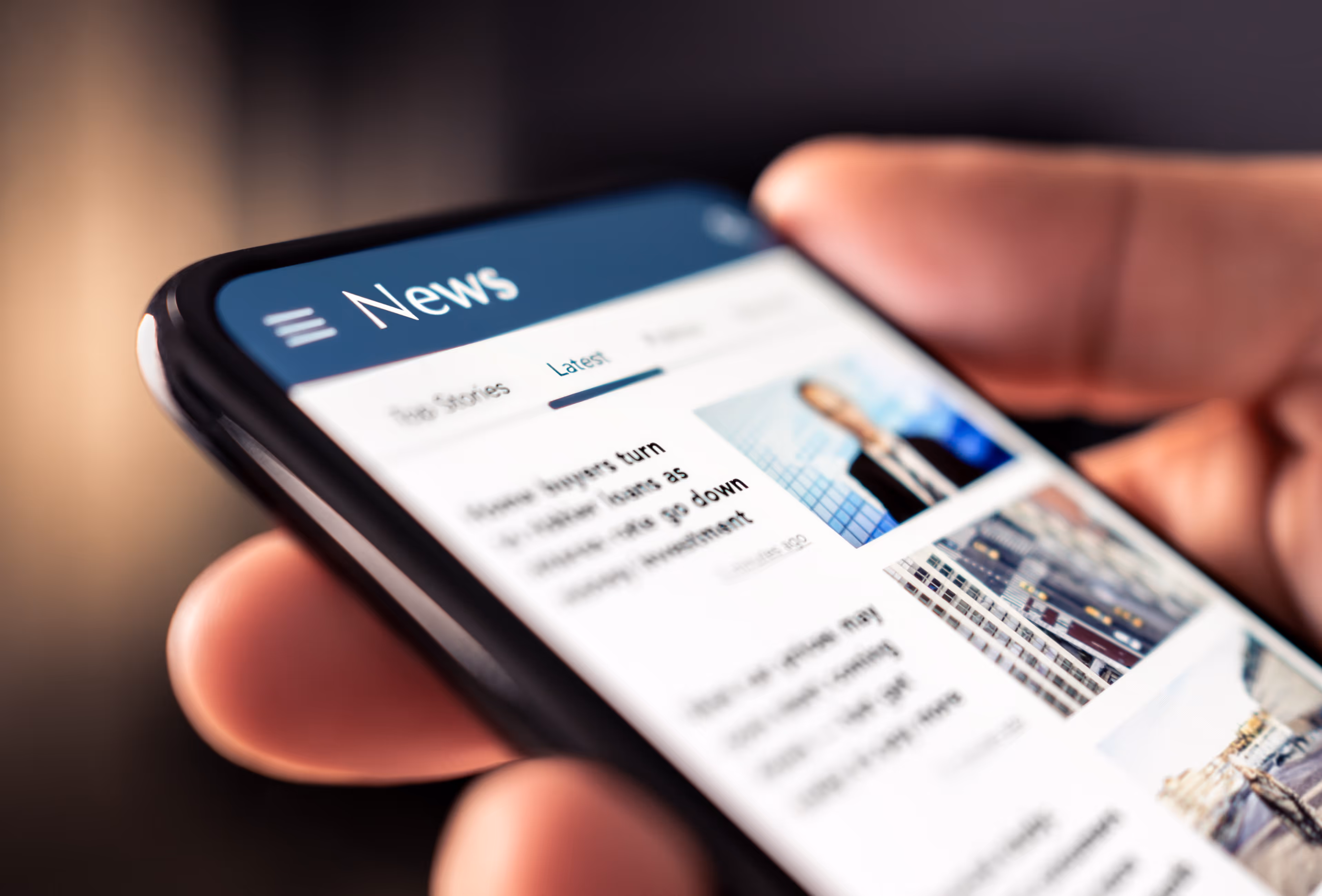 Close-up of a hand holding a smartphone displaying a news app with headlines and images.
