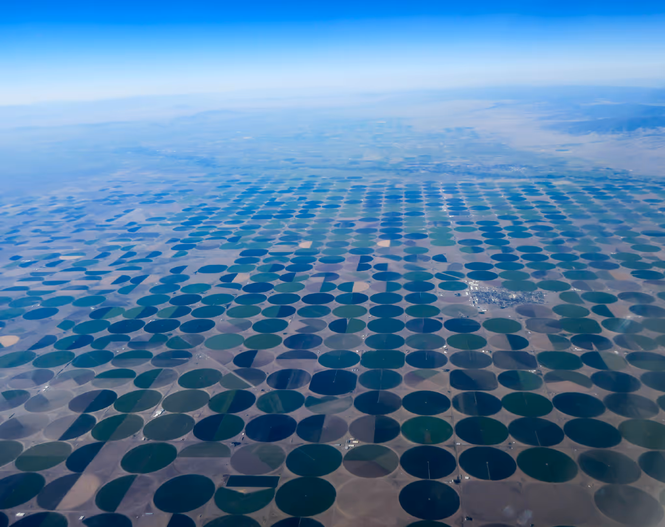 Aerial view of circular crop fields arranged in a grid pattern under a clear blue sky.