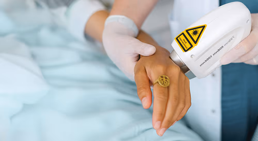 Eine Ärztin lasert den Handrücken einer Patientin, die auf dem Behandlungsstuhl liegt.