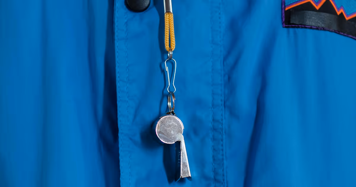 A silver whistle attached to a yellow landyard is dangling on top of a bright blue parka. 