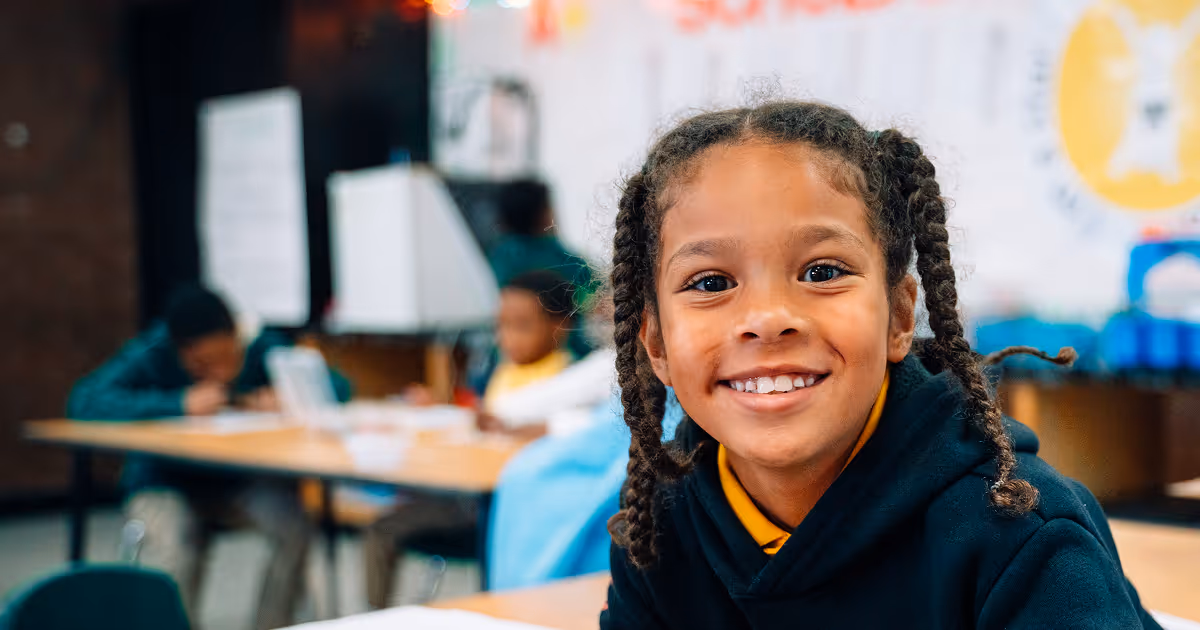 A cheesy Tulsa Legacy scholar is grinning at the camera. A white board and other scholars are in the background. 