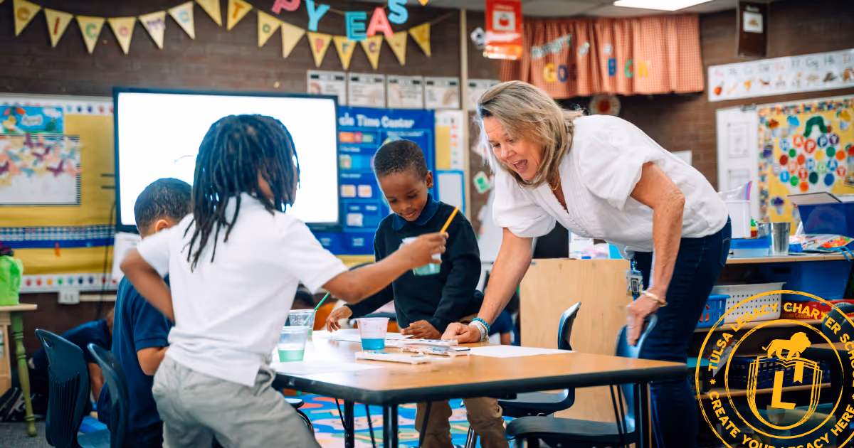A TLCS teacher is smiling at a table of PreK scholars who are painting. The TLCS stamp in yellow is in the lower righthand corner.