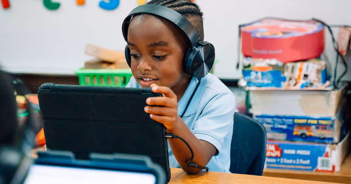 A Primacy Academy student is smiling at an iPad while wearing headphones.