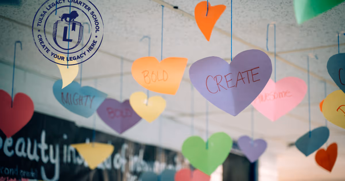 The word "CREATE" is written on a purple, paper heart with other positive words in the background. The paper hearts are hanging from blue string from a classroom ceiling.