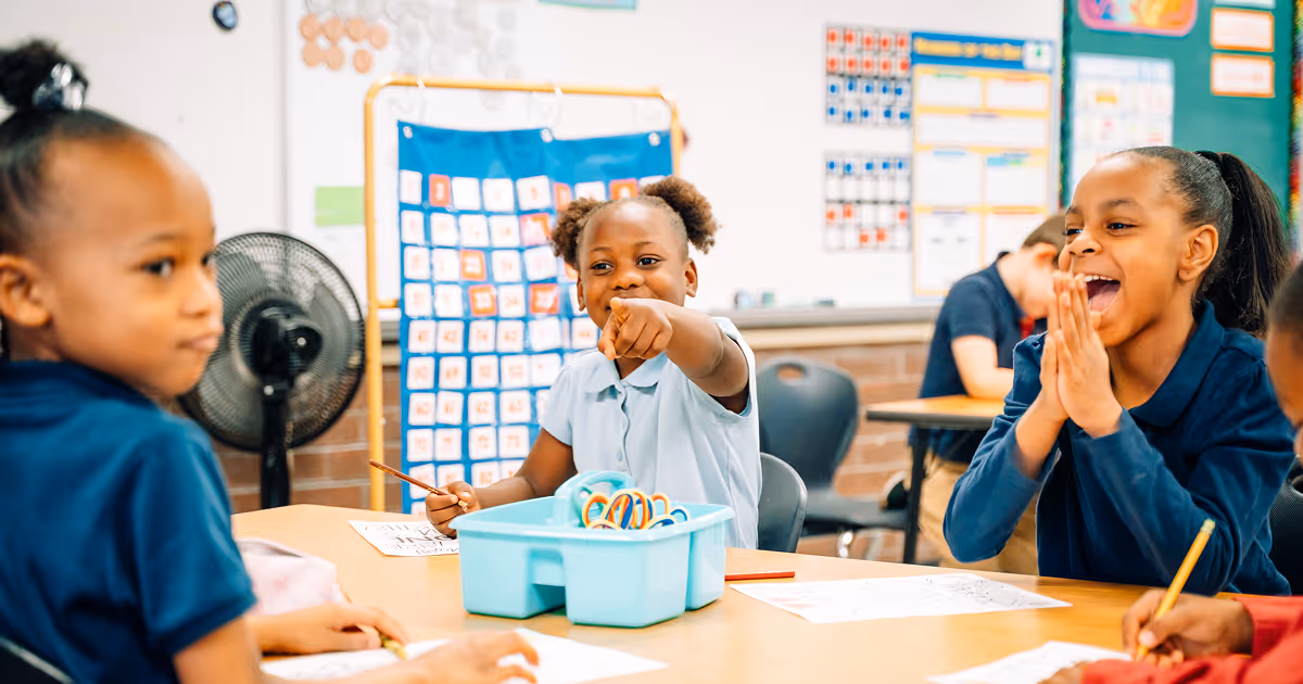 A group of primary academy students laughing. The student in focus is excitedly pointing at the camera.