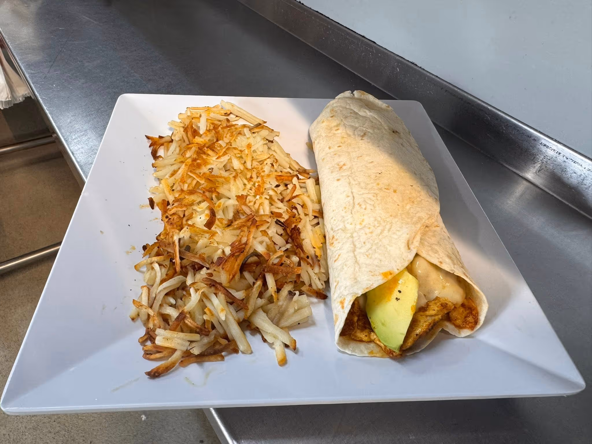 A white plate with a burrito and a side of hash browns.