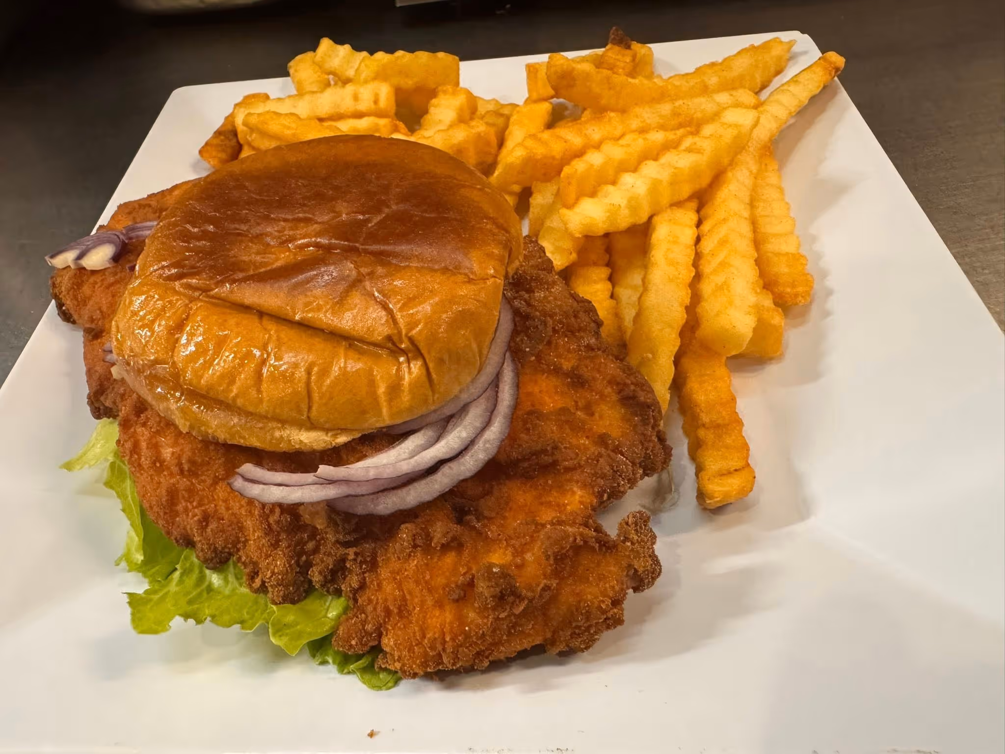 A chicken sandwich with onions and fries on a white plate.
