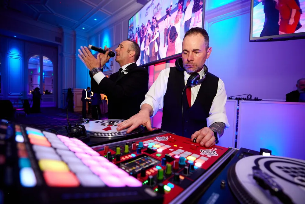 Wedding DJ mixing on turntables with headphones while an MC sings with the crowd, wedding DJ service