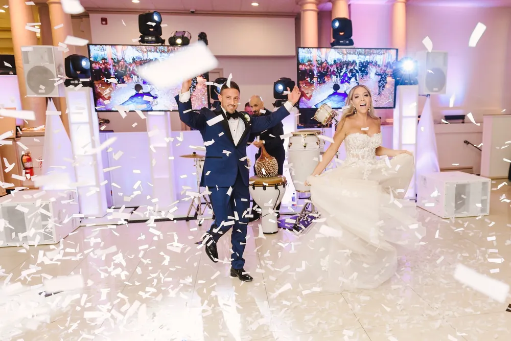 Bride and groom dancing in a shower of white confetti from confetti cannons in front of the DJ setup