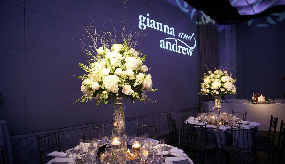 Custom monogram reading "gianna and andrew" projected on a wall above white floral wedding centerpieces