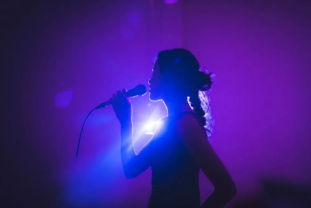 Wedding vocalist singing into a microphone, silhouetted in purple and blue stage light