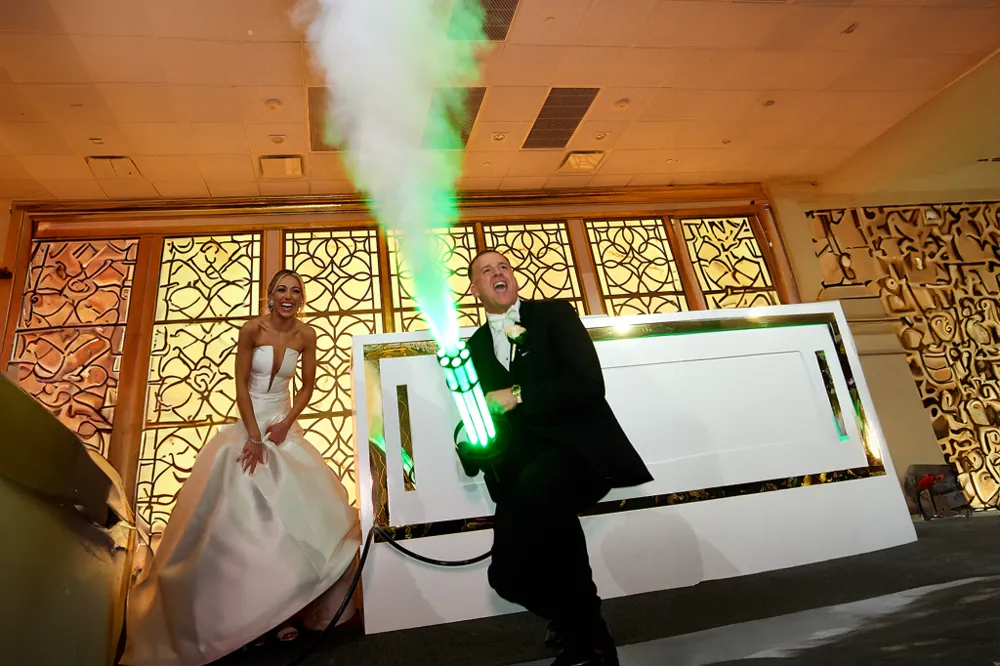 Groom firing a green-lit CO2 gun on the dance floor as the bride smiles beside him, a party effect add-on