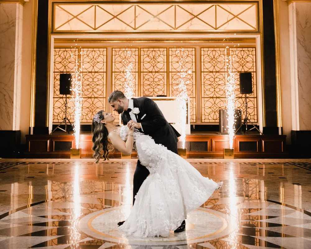Groom dipping the bride on a marble floor as cold spark fountains glow behind them, a first dance effect