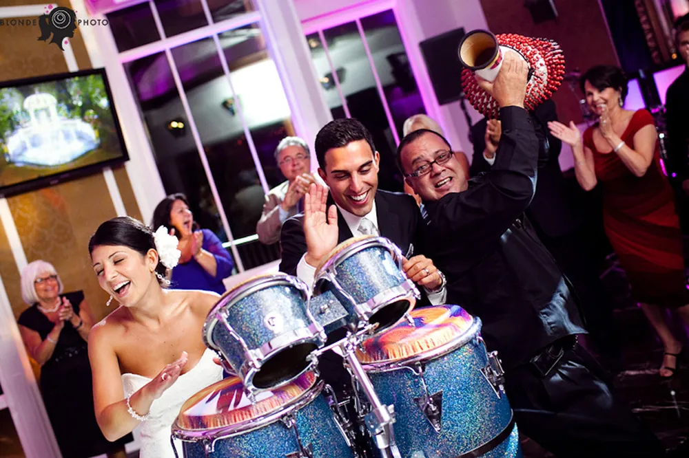Bride, groom and guests playing glittery blue timbales with a percussionist on the dance floor