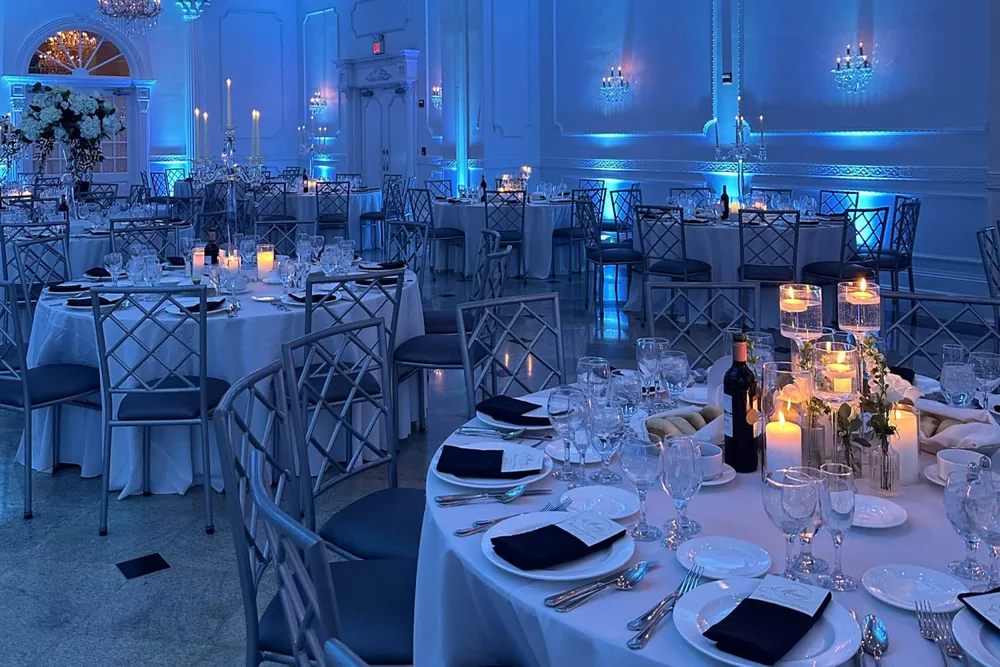 Ballroom tables set with candles and glassware, washed in blue wedding uplighting along the walls