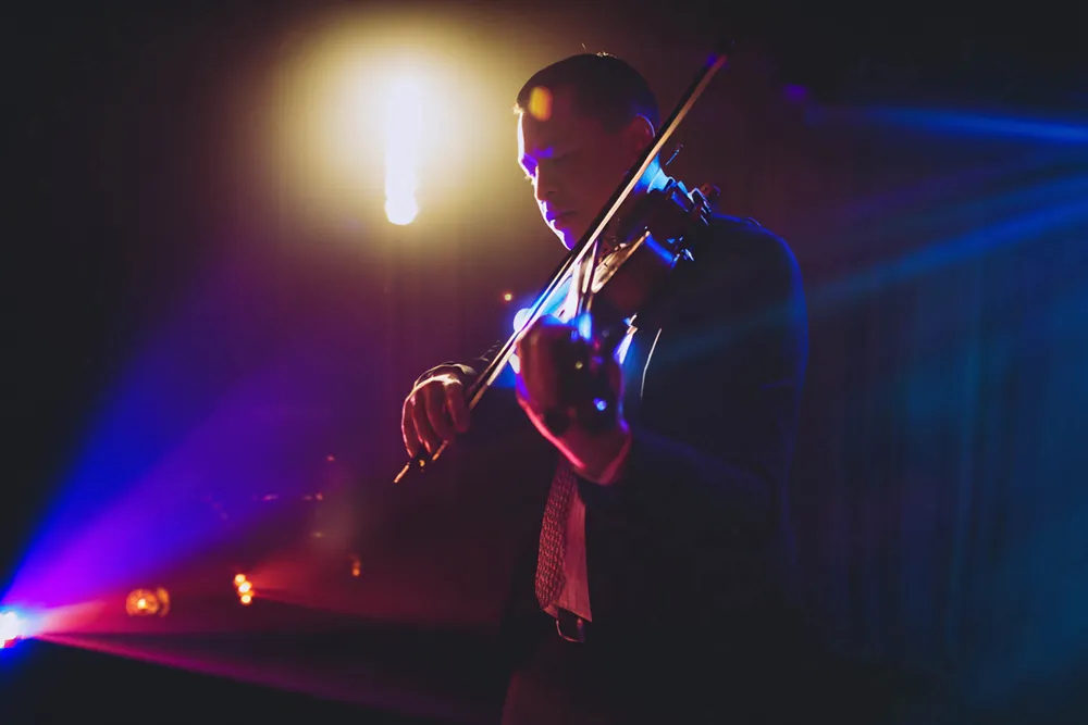 Electric violinist playing under purple and gold stage lights, a live music add-on for receptions
