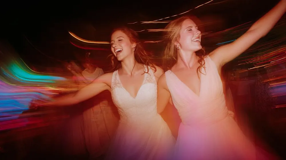 Two bridesmaids dancing and laughing with light trails swirling around them on a dance floor