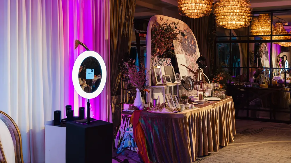 Open-air photo station with a ring-light camera beside a decorated table of props and frames