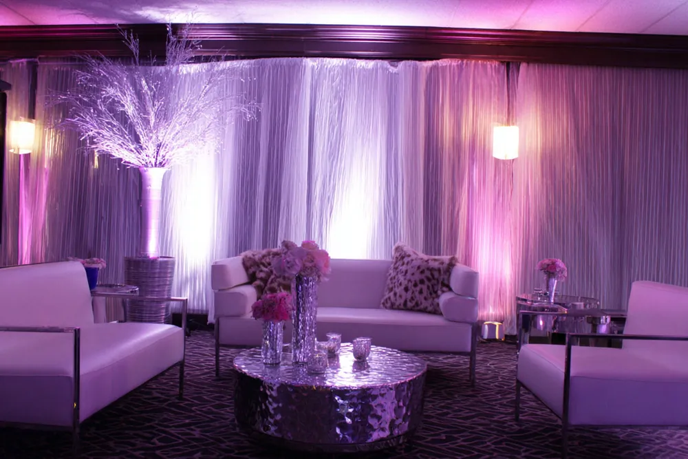 Lounge decor with white sofas, a hammered silver table and draped walls lit pink and white