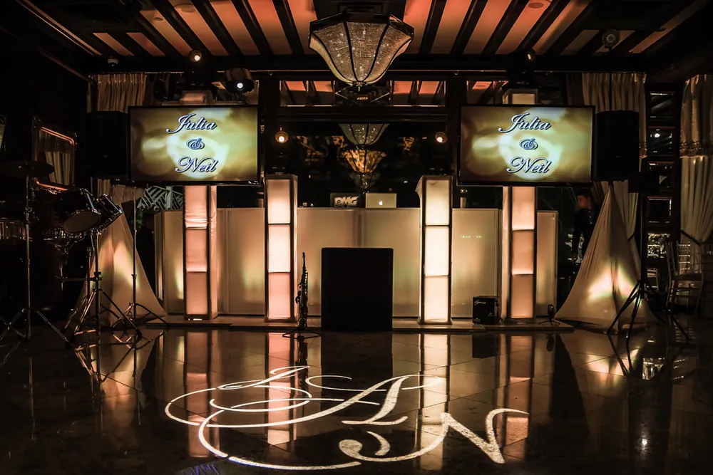 DJ setup with two video displays showing the couple's names and a monogram lit on the dance floor