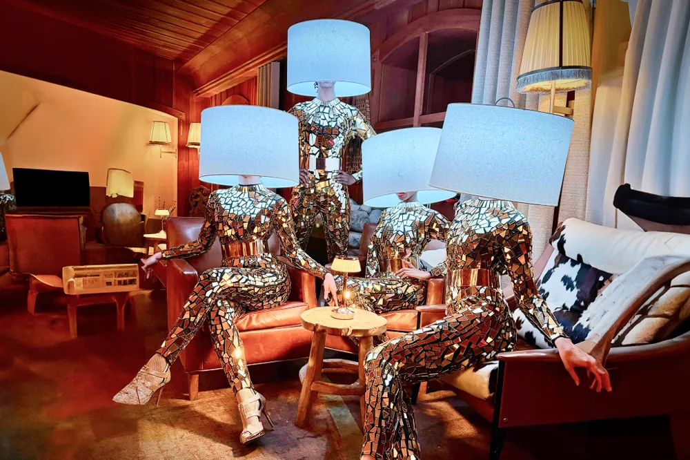 Performers in mirrored costumes with lampshades on their heads posing as living lamps in a lounge