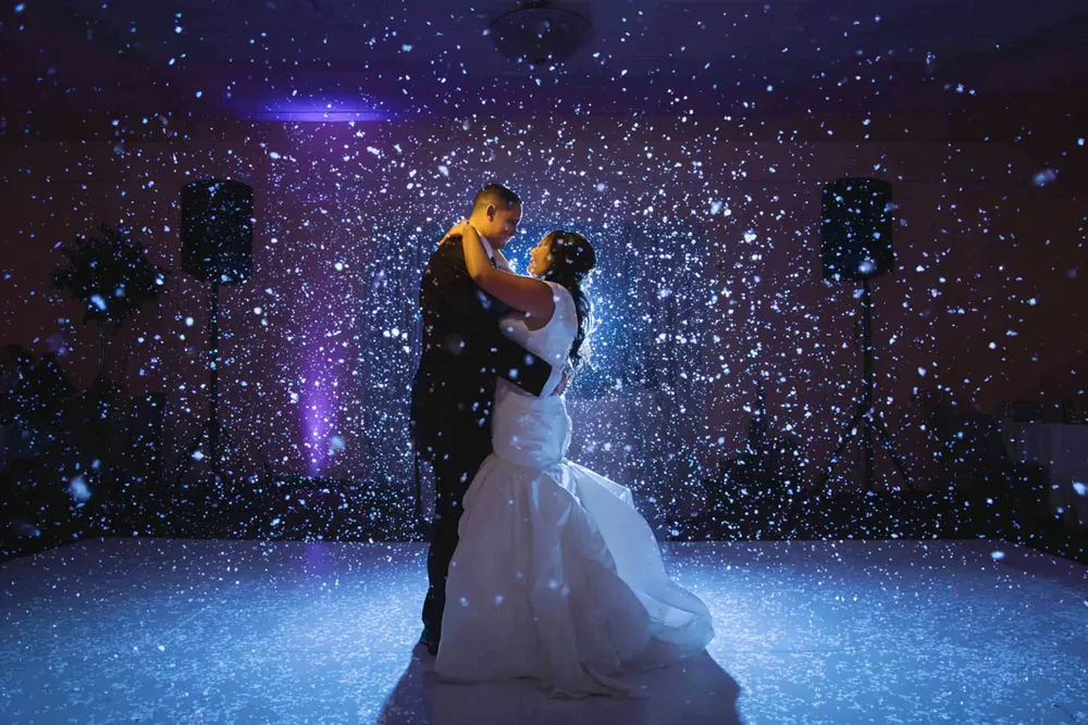 Bride and groom slow dancing while falling snow effect glows in blue light around them
