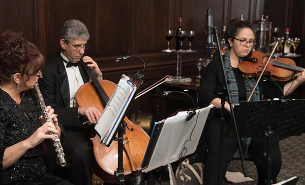 Flute, cello and violin trio playing live ceremony music from sheet music at a wedding