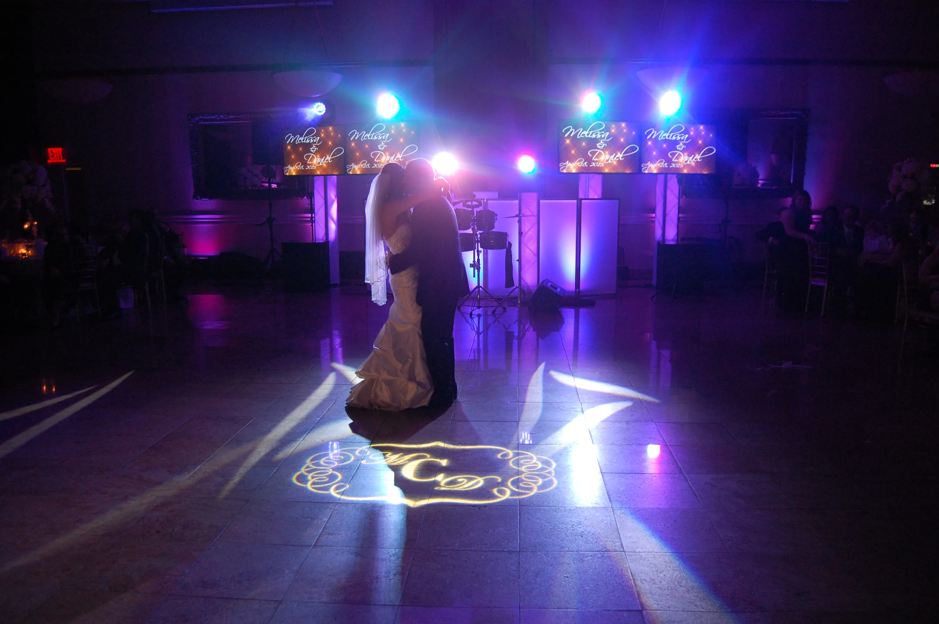 Newlyweds sharing a first dance in a spotlight with a custom monogram projected on the dance floor