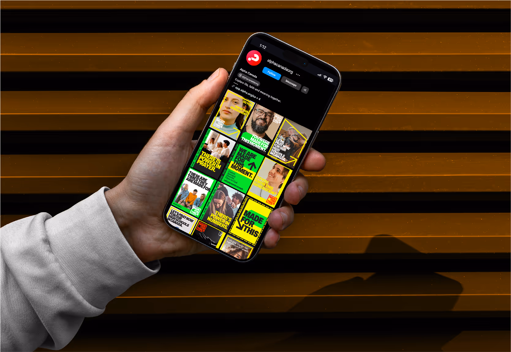 A hand holding an iPhone displaying the Alpha Canada Instagram grid.