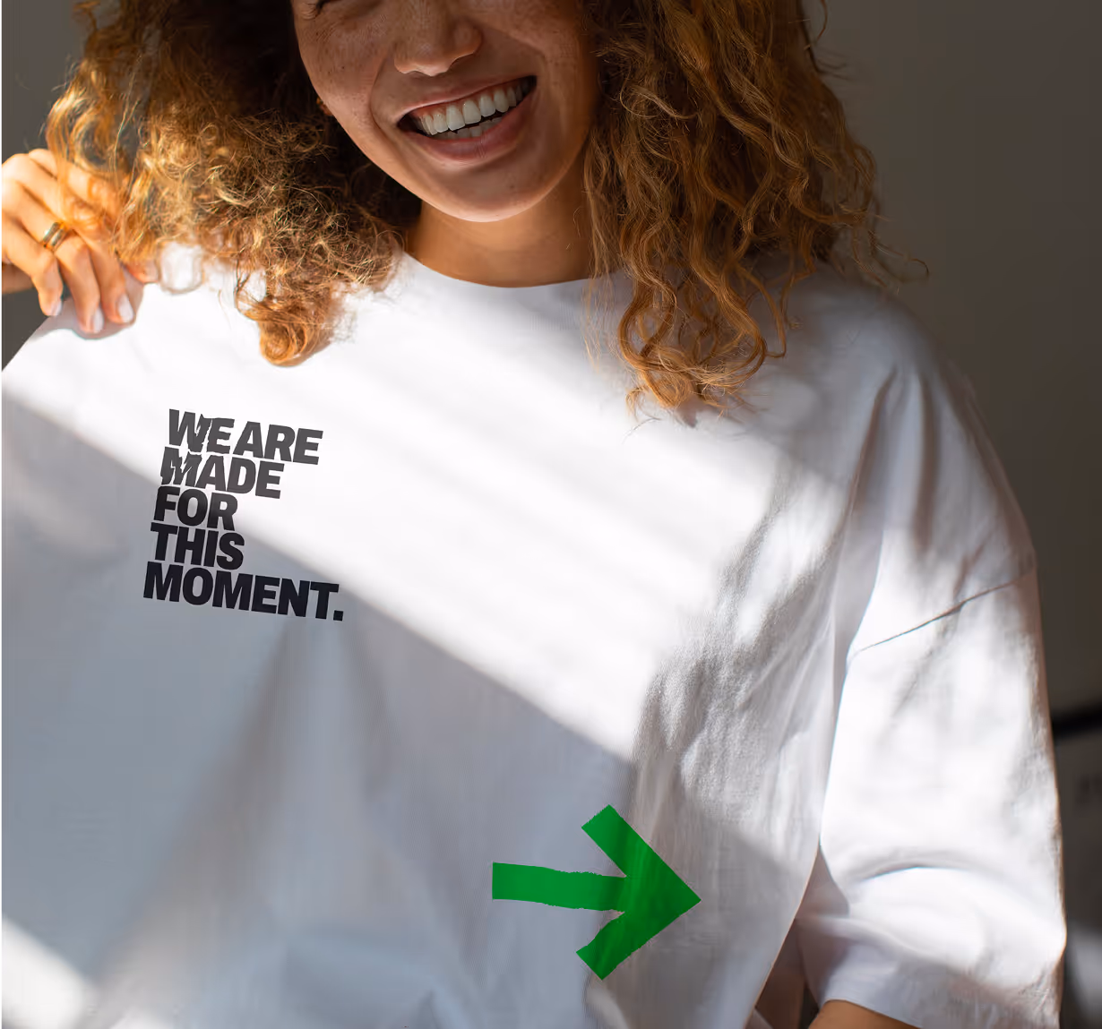 A photo of a smiling, curly haired lady wearing the Made For This campaign merchandise t-shirt. 