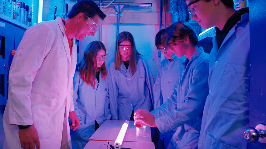 An image of a teacher and his students looking at a science experiment.