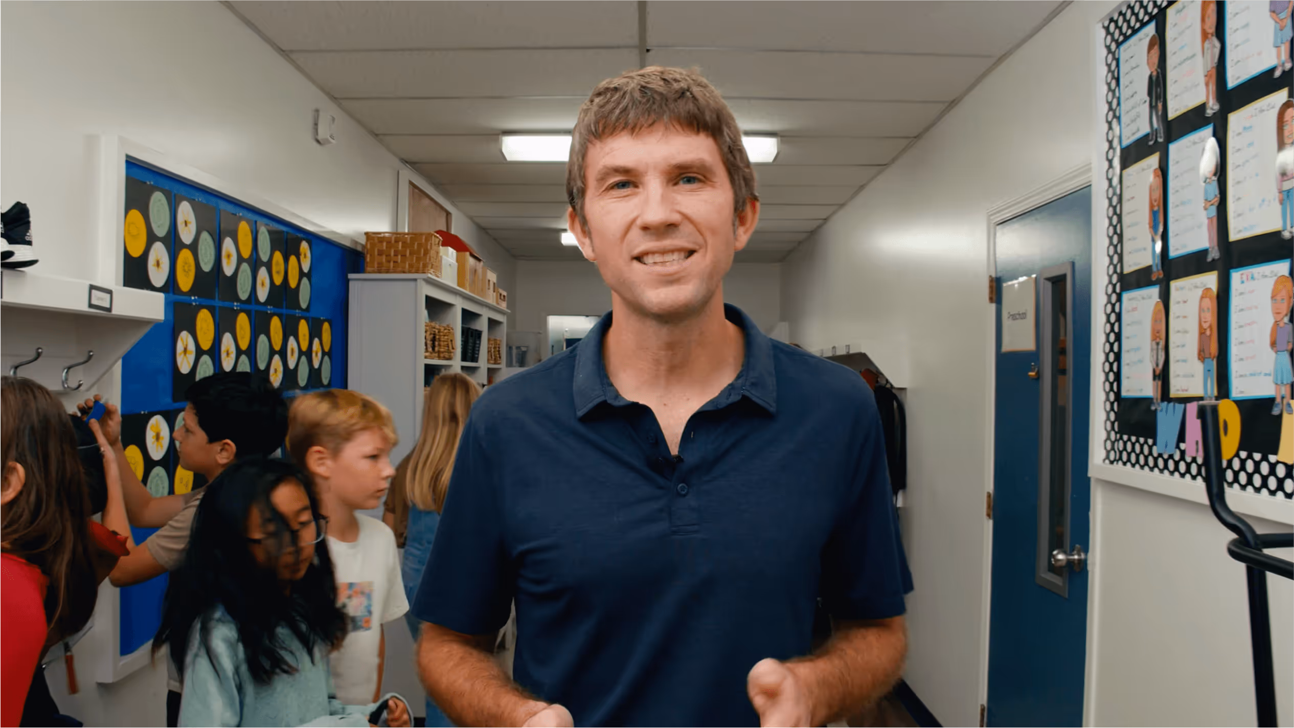 An image of a middle aged man walking through a hallway talking to the camera.