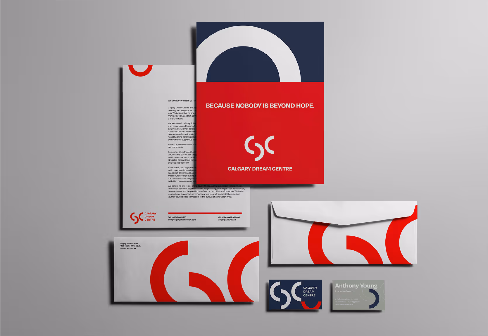 Stationery set with Calgary Dream Centre branding including letterhead, envelopes, folder with slogan 'Because nobody is beyond hope,' and business cards featuring red and navy circular design elements.