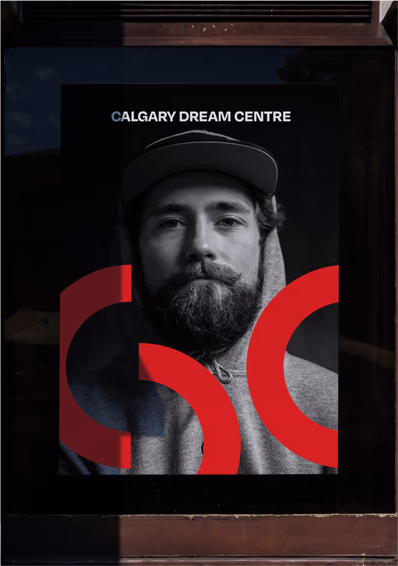 Black and white poster of a bearded man wearing a hoodie and a cap with the text 'CALGARY DREAM CENTRE' and red abstract shapes.