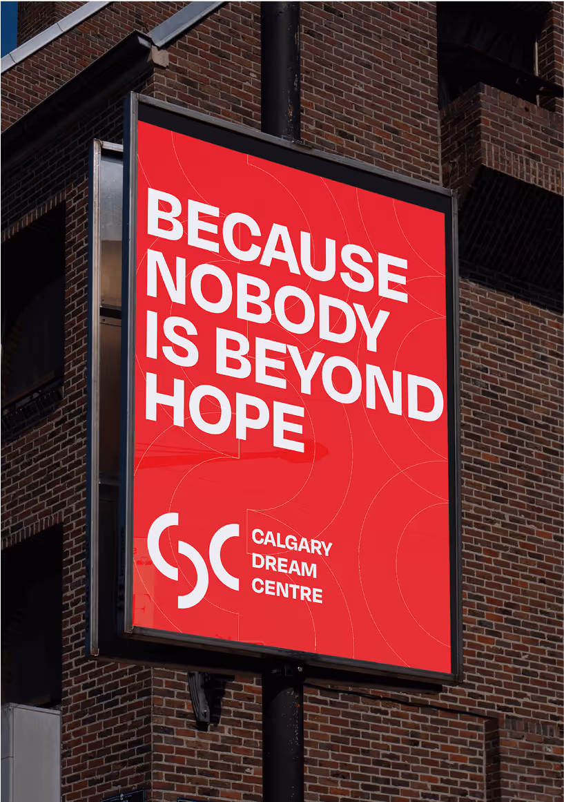 Red billboard on a street pole with white text reading 'Because nobody is beyond hope' and logo for Calgary Dream Centre.