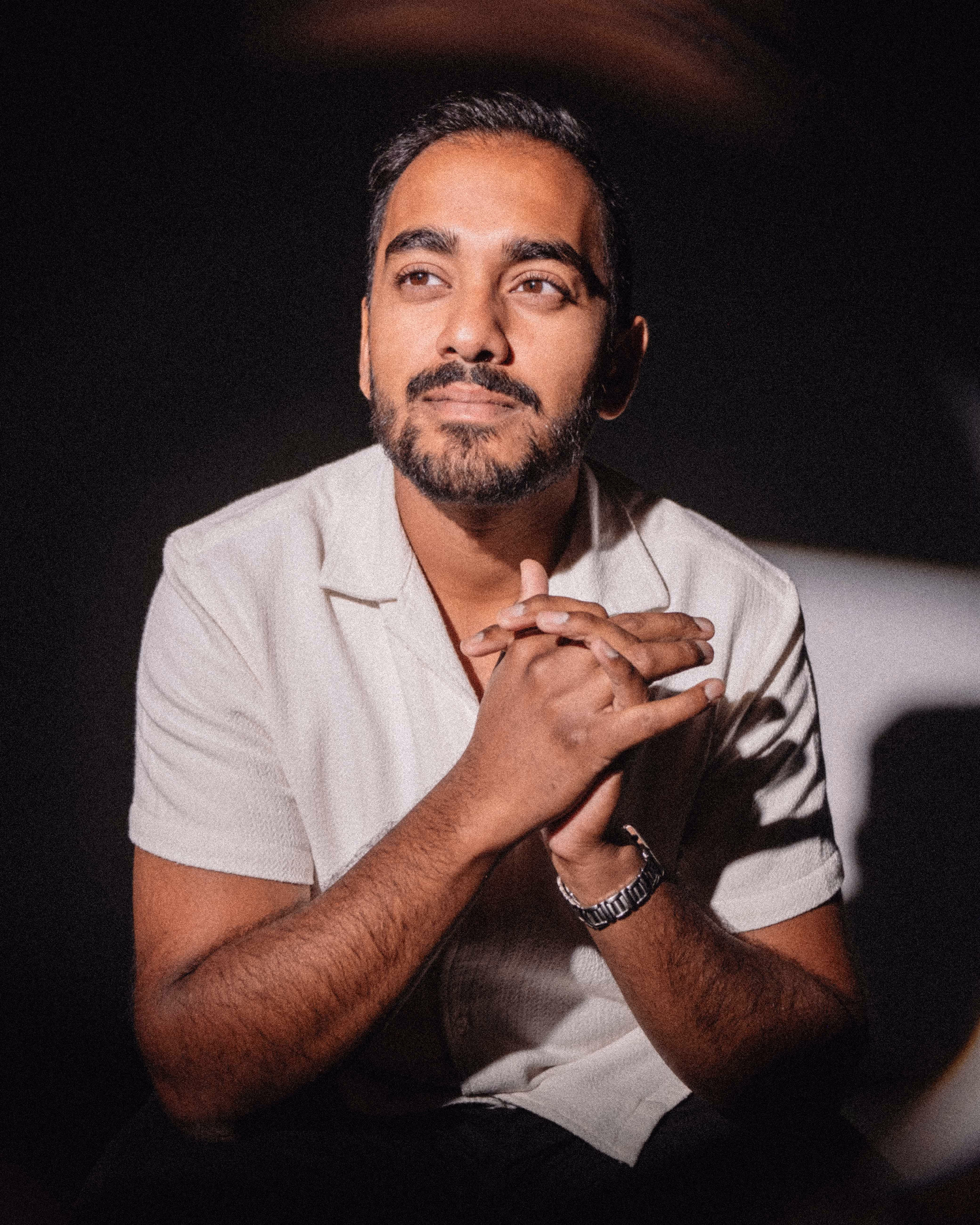 A bearded man holding his hands together and looking into the distance