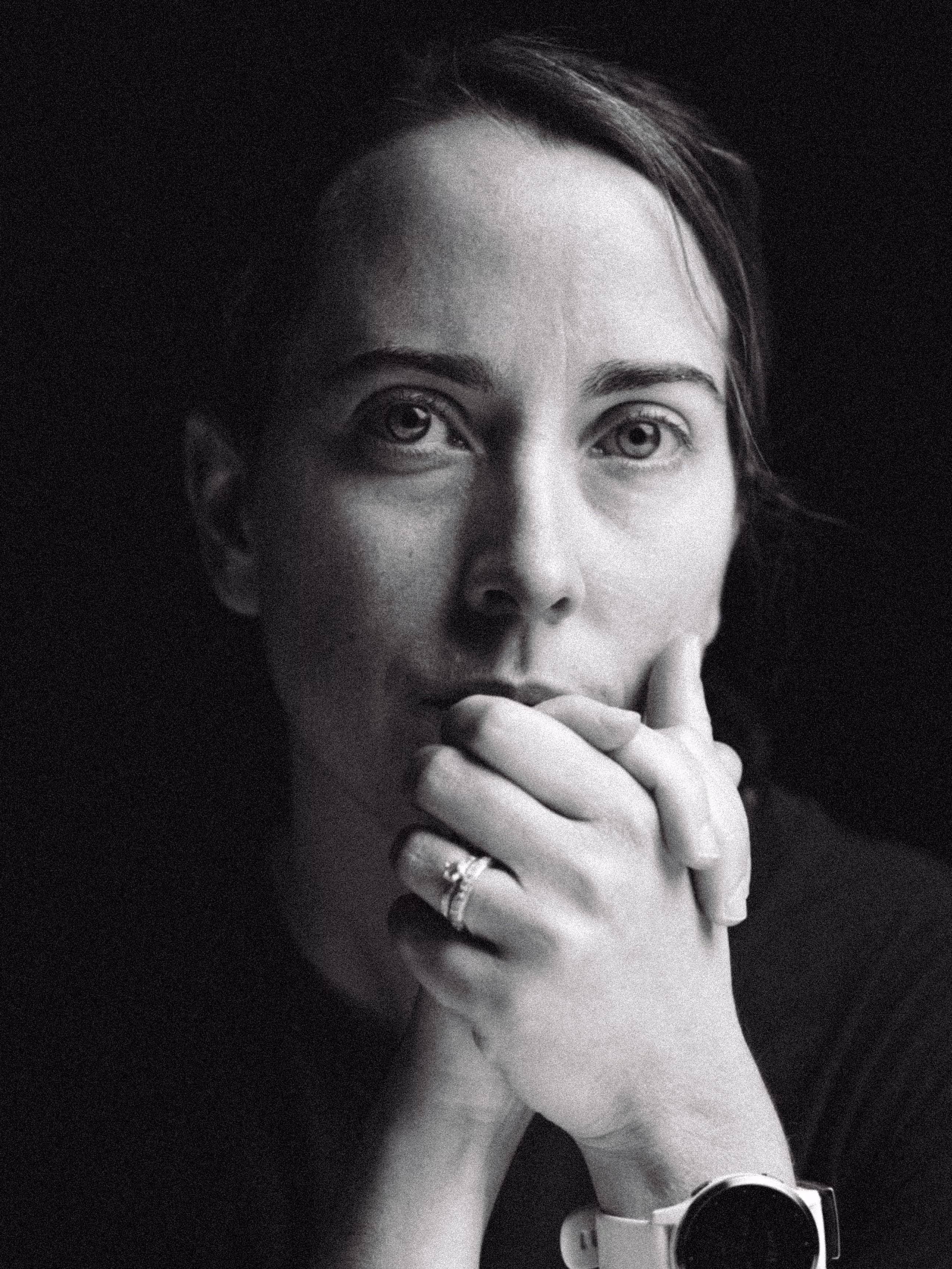Black and white close-up portrait of a thoughtful woman resting her chin on clasped hands, wearing a ring and a smartwatch.