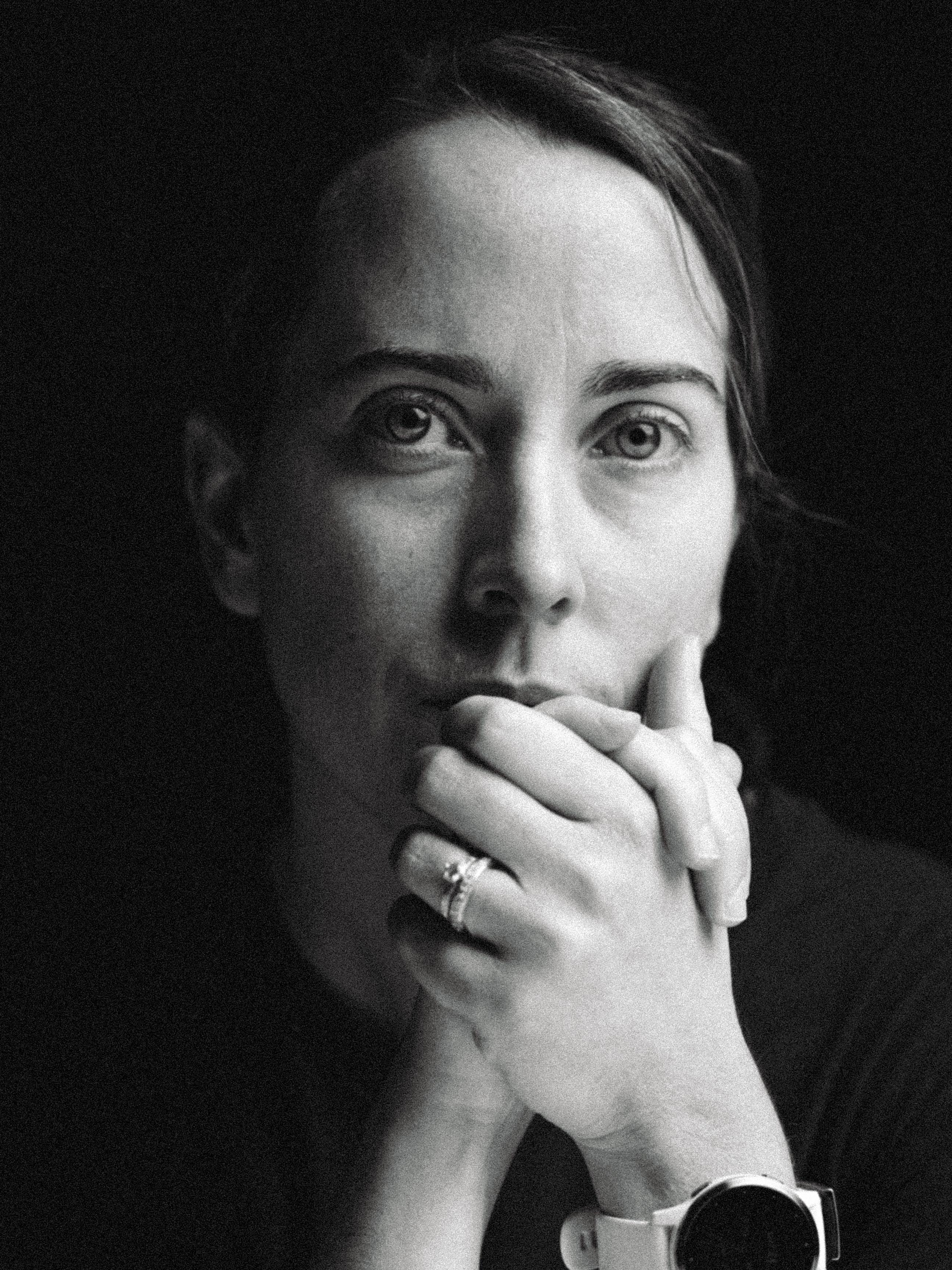 Black and white close-up portrait of a thoughtful woman resting her chin on clasped hands, wearing a ring and a smartwatch.
