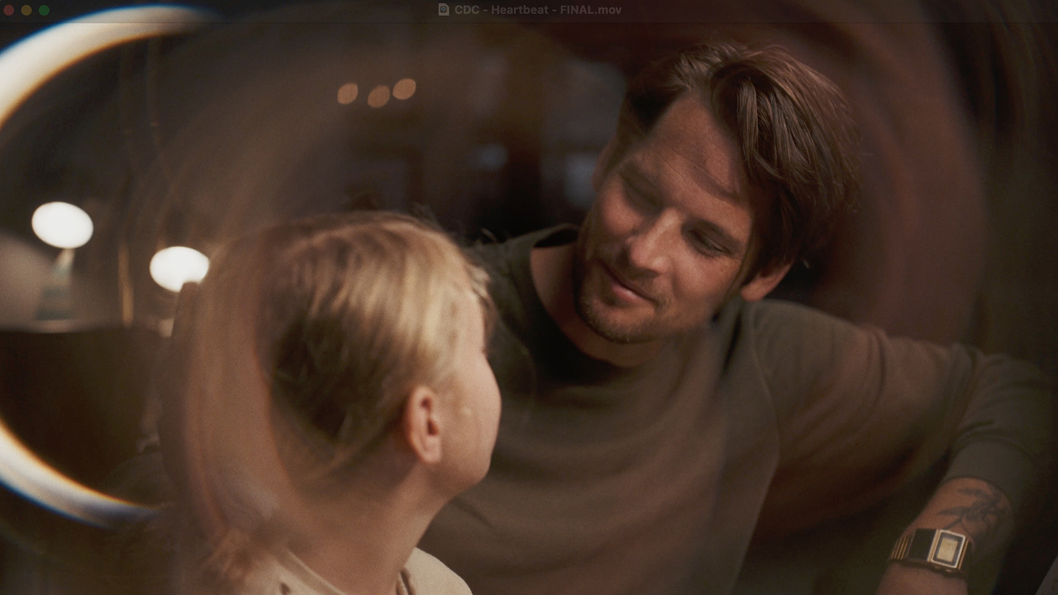 Man with a beard and wristwatch smiling warmly at his young daughter in a softly lit room.