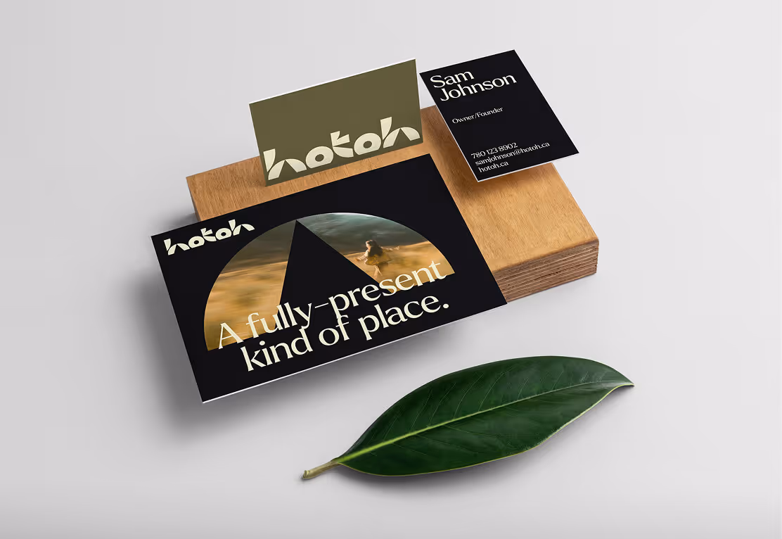 Set of business cards and a postcard with 'hotoh' branding and slogan 'A fully-present kind of place' on a wooden block, next to a green leaf.